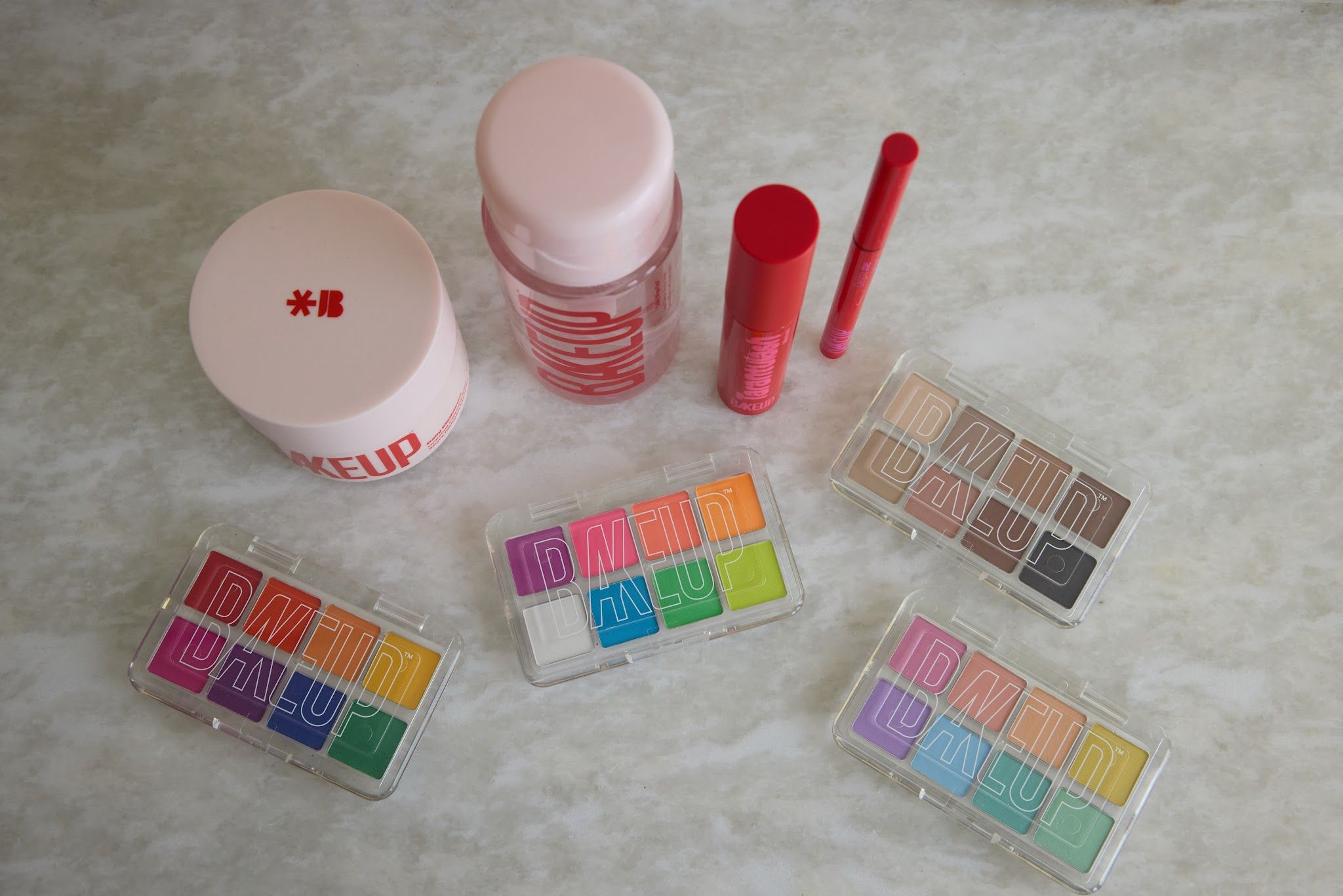 Complete vegan makeup kit flat lay from Bakeup Beauty: cleansing balm, makeup remover, Tarantulash mascara, eyeliner and four Micro Palm eyeshadow palettes