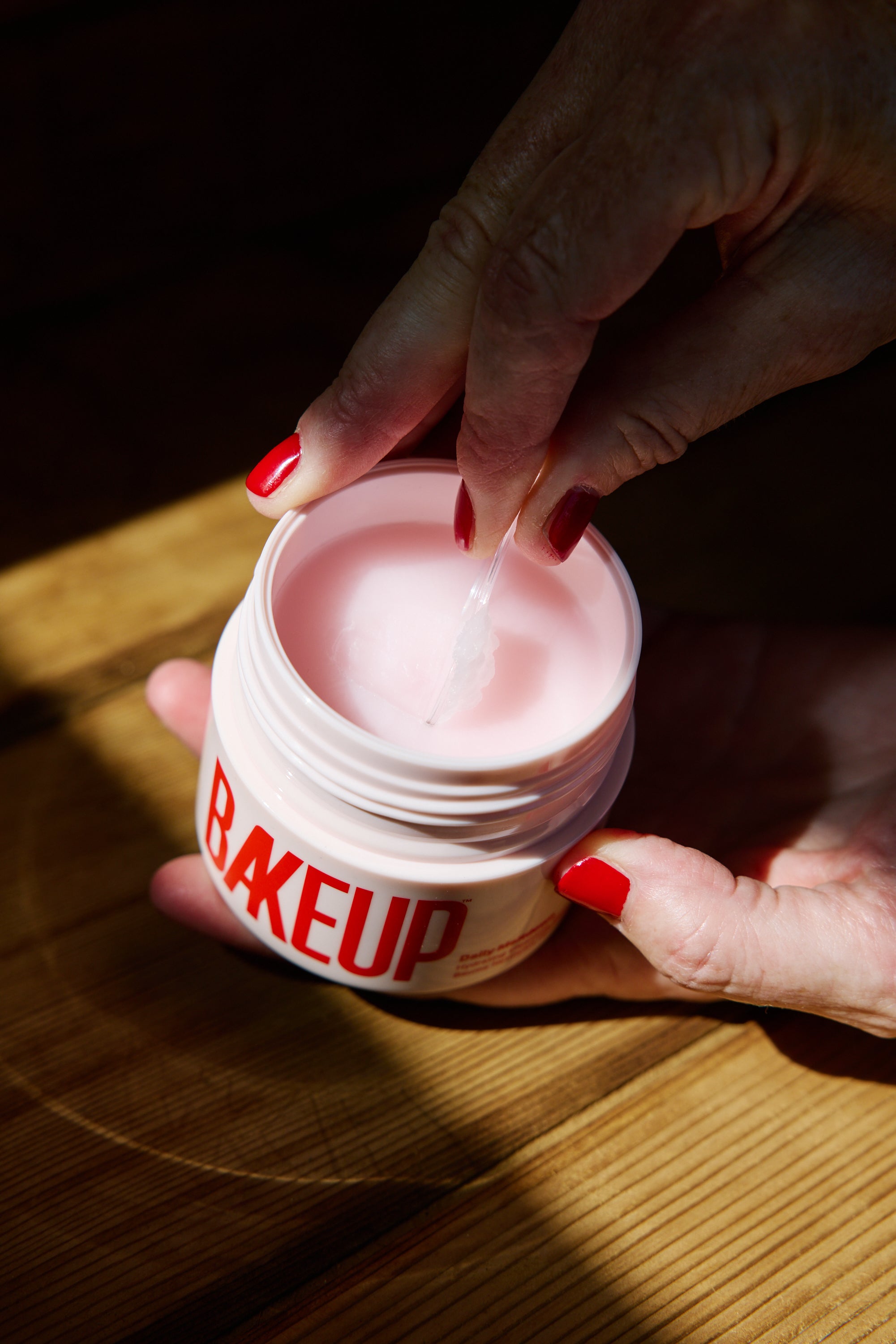 Hands scooping BAKEUP Daily Meltdown cleansing balm from the jar to remove waterproof mascara