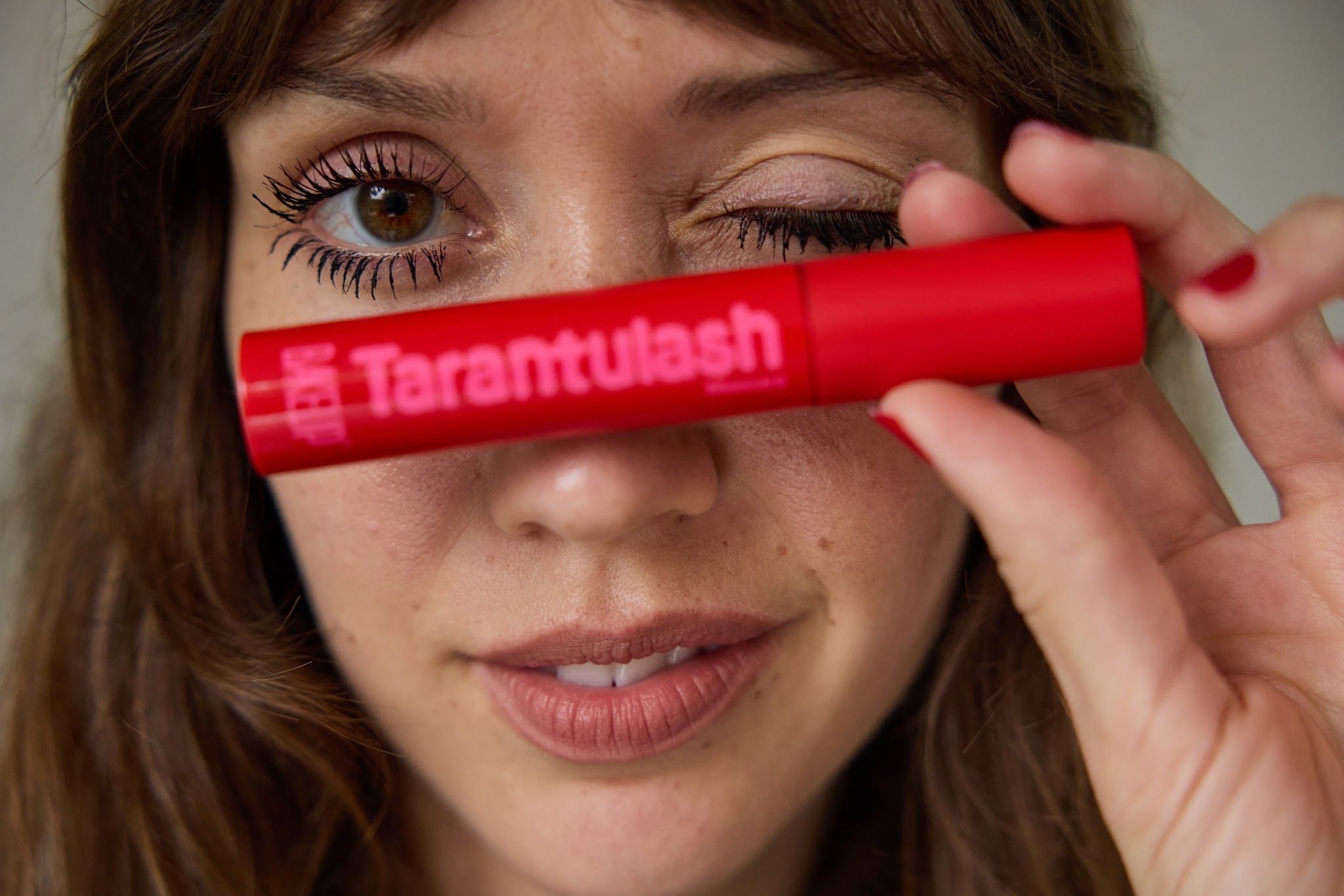 Woman holding a red Tarantulash vegan mascara tube across her face, showing separated, clump-free lashes