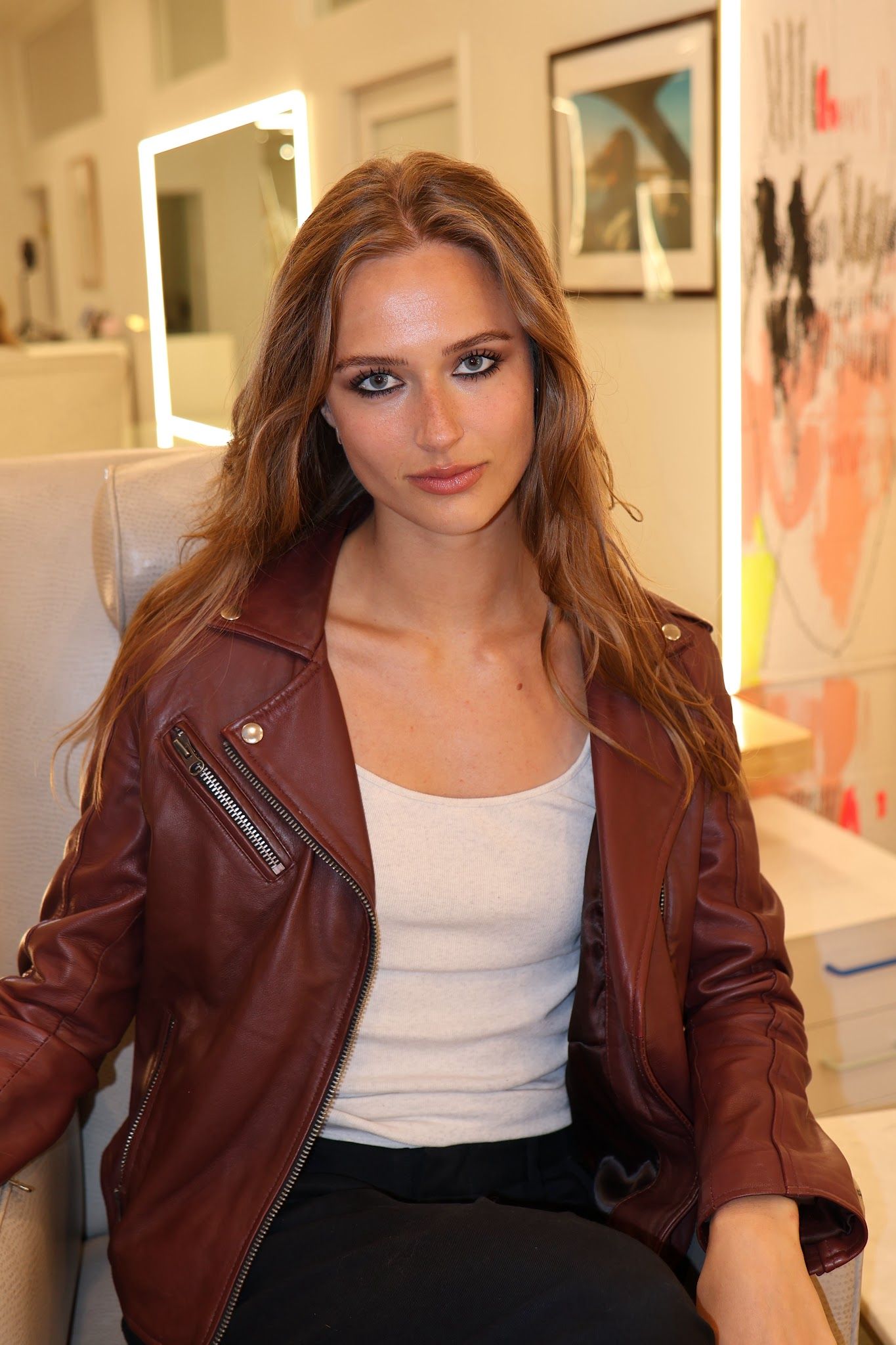 Woman with tightlined, intensely defined eyes, long auburn hair and a burgundy leather jacket
