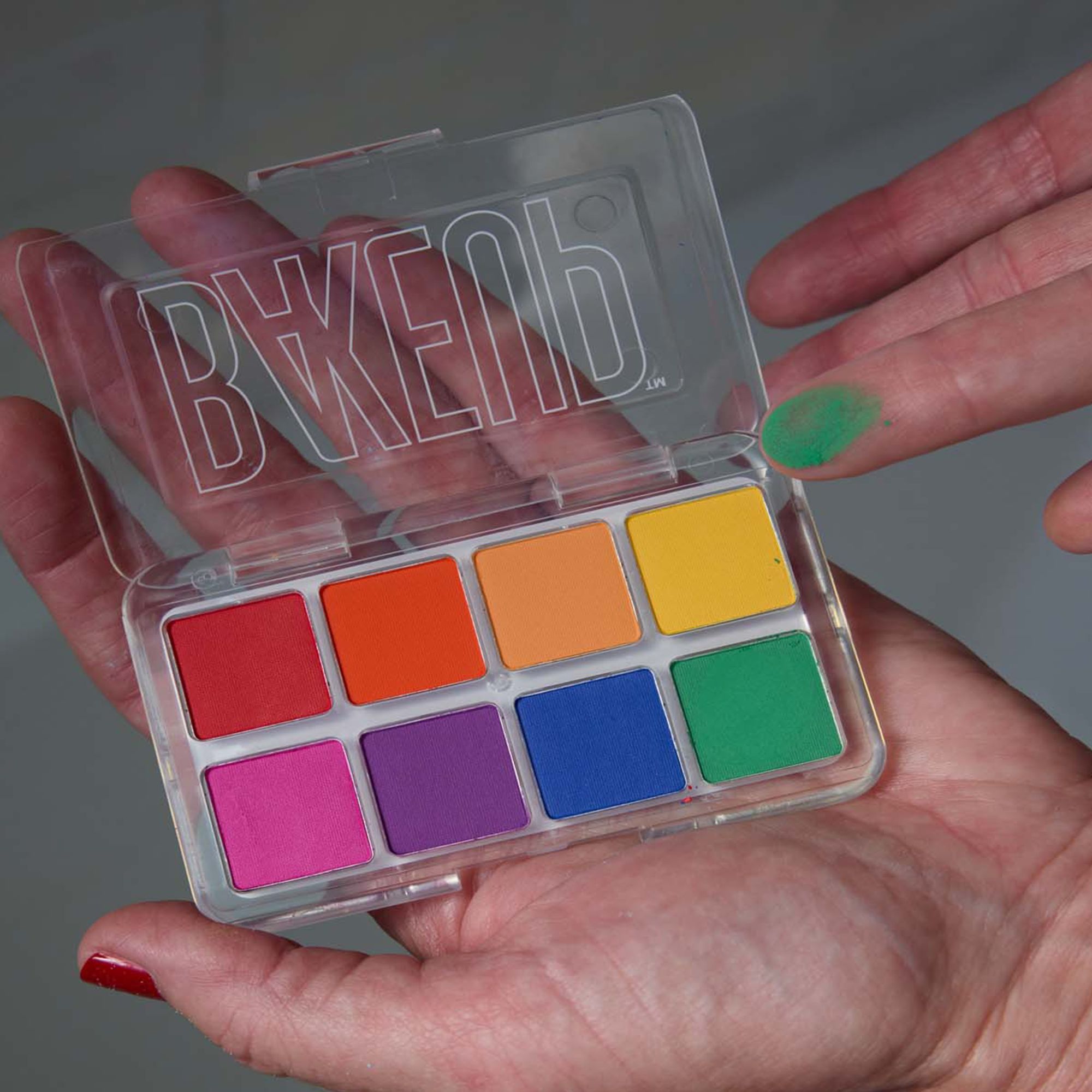 Hand holding the open Bakeup Beauty Primary Micro Palm eyeshadow palette with eight bright matte shades