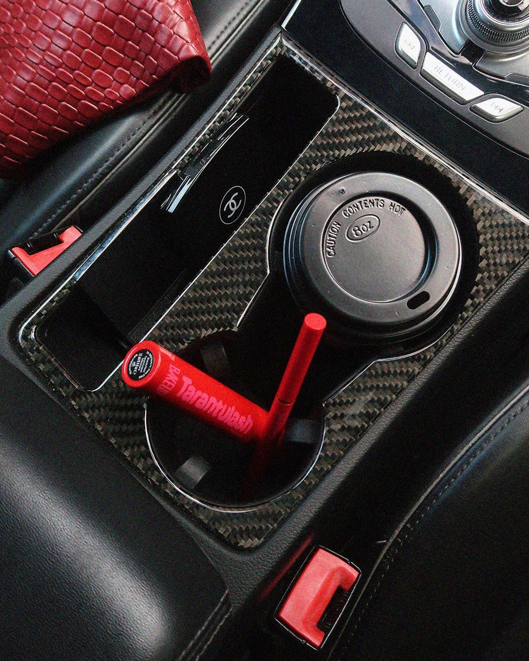 Tarantulash mascara next to a coffee cup in a car cup holder, a real-life on-the-go makeup routine