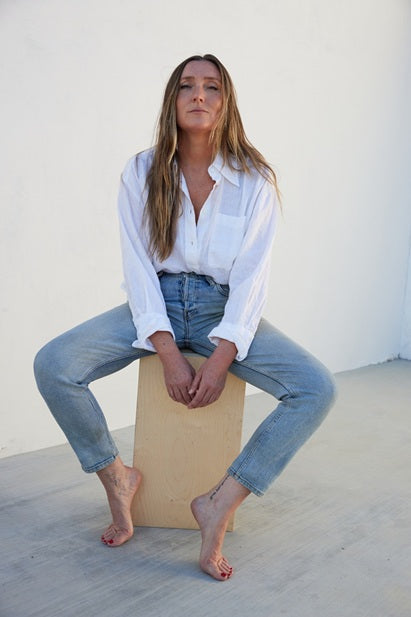 Woman sitting on a box wearing a white shirt and blue jeans against a white background