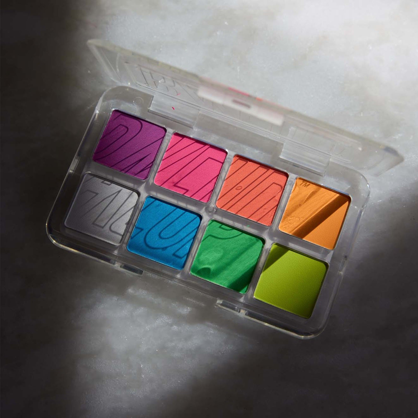 Set of neon eyeshadow palette in a clear plastic case on a textured surface
