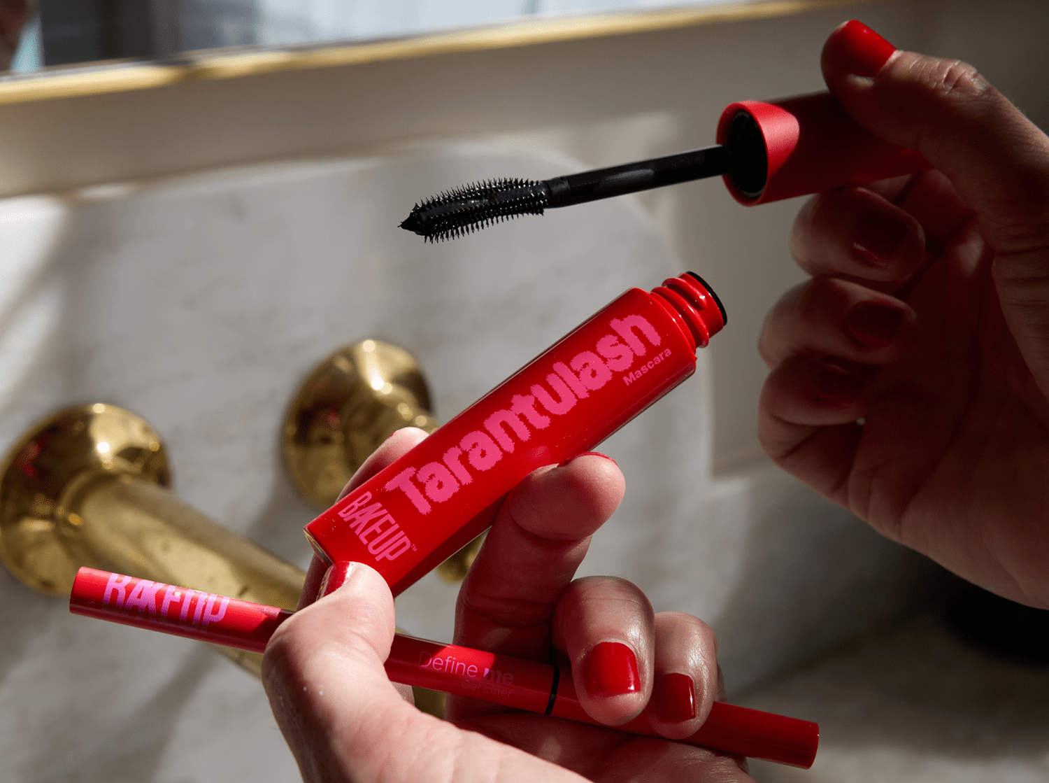Red mascara tube labeled 'Tarantulash' held by a person with a blurred background.