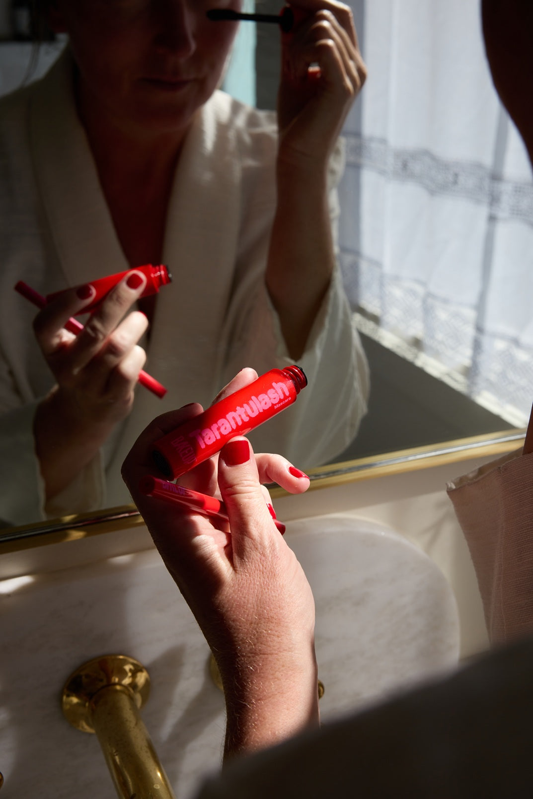 Person applying mascara in front of a mirror with a red mascara tube.